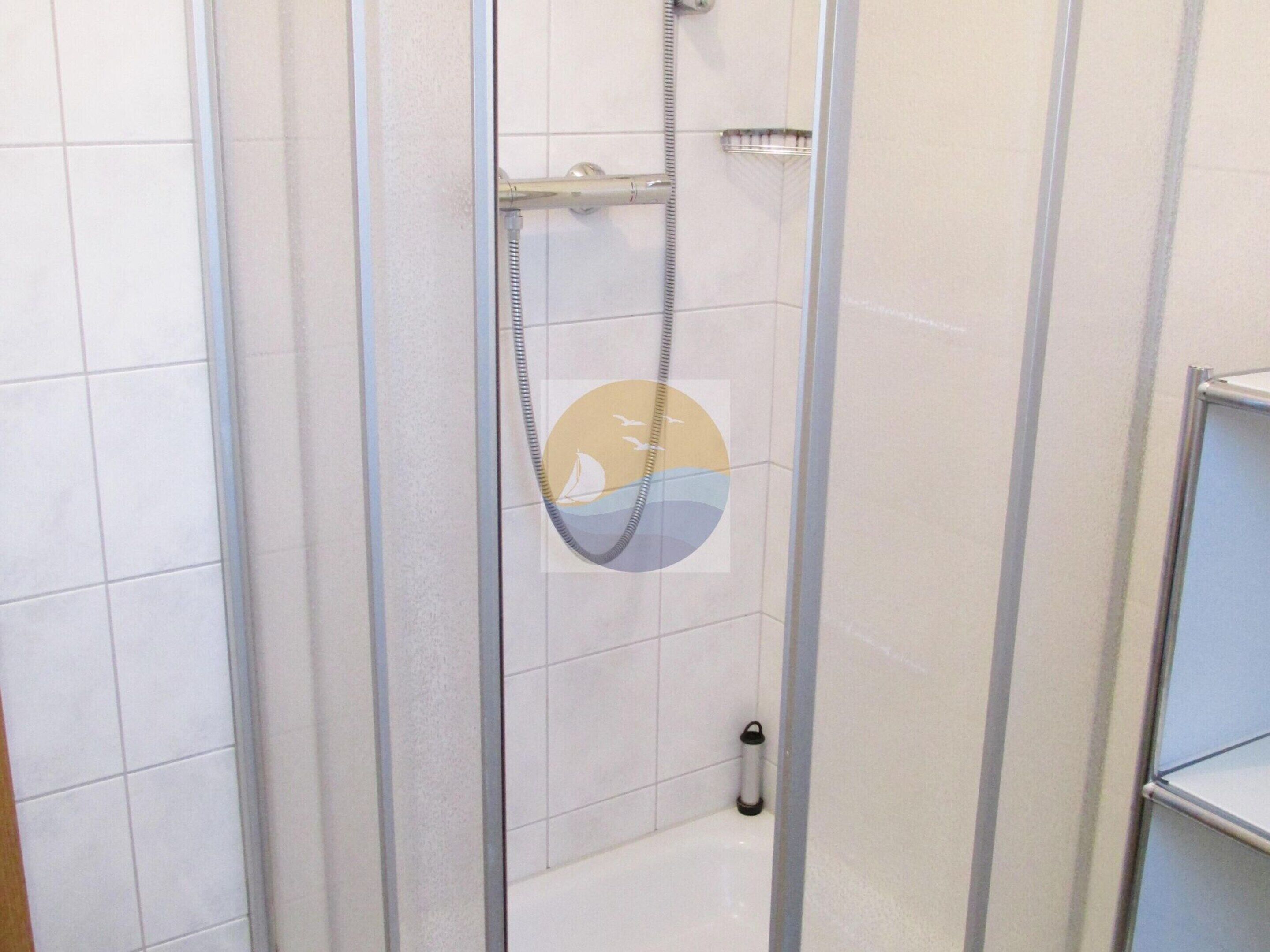 A shower enclosure with a glass door, a handheld showerhead, and a small shelf.
