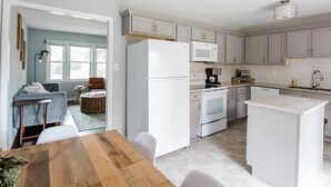 A modern kitchen with white appliances, a dining area with a wooden table, and a view into a living room with a sofa and a rug. - HOT TUB, Fenced in Yard, Pet Friendly, Game room (Fayetteville)