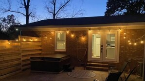 A patio area with a hot tub, a wooden deck, and string lights. - HOT TUB, Fenced in Yard, Pet Friendly, Game room (Fayetteville)