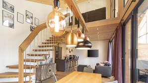 Un intérieur moderne avec un escalier en bois, un coin repas doté d’une table en bois et un espace de vie comprenant un canapé et un téléviseur.