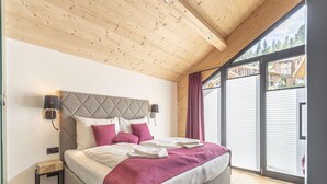 Une chambre avec un grand lit, un plafond en bois et une vue sur un ensemble de chalets en bois, visible à travers une porte coulissante.