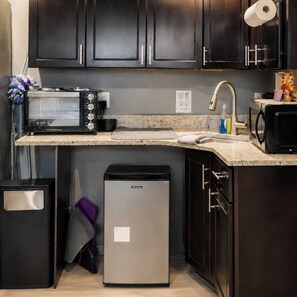 A compact kitchen with a microwave, toaster, sink, and a small refrigerator.