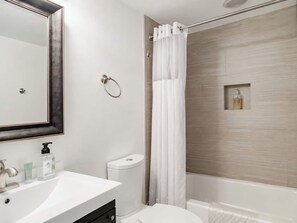 A modern bathroom with a white sink, a toilet, a shower with a curtain, and a mirror with a black frame.