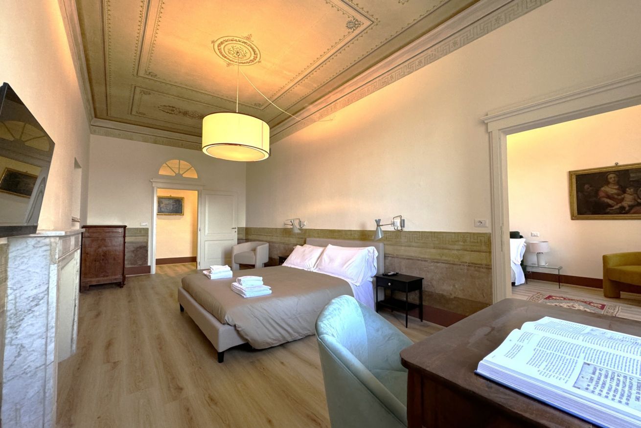 A hotel room with a large bed, a desk, a chair, a nightstand, and a ceiling with decorative molding.