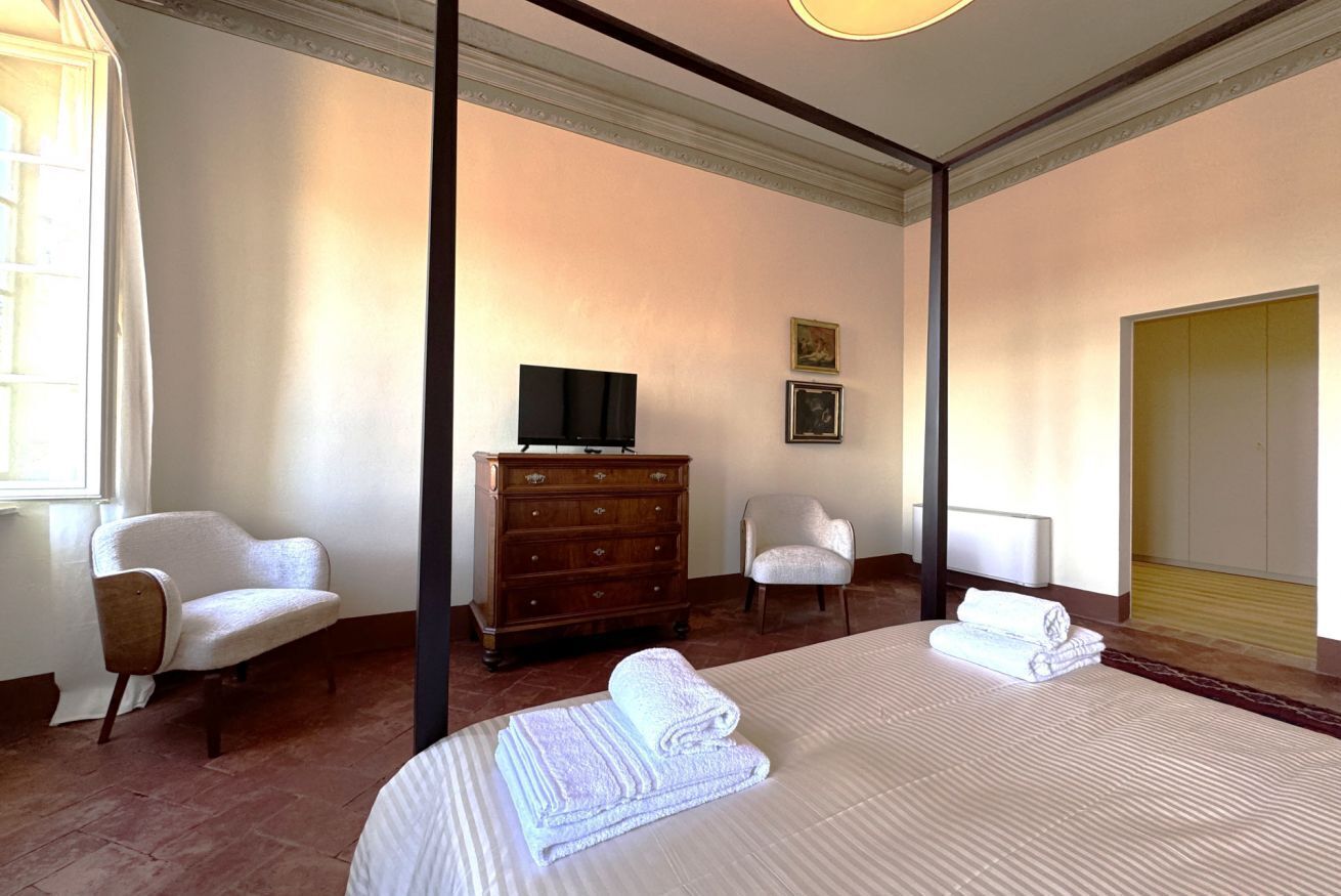 A hotel room with a large bed, two chairs, a dresser, a television, and a window with curtains.