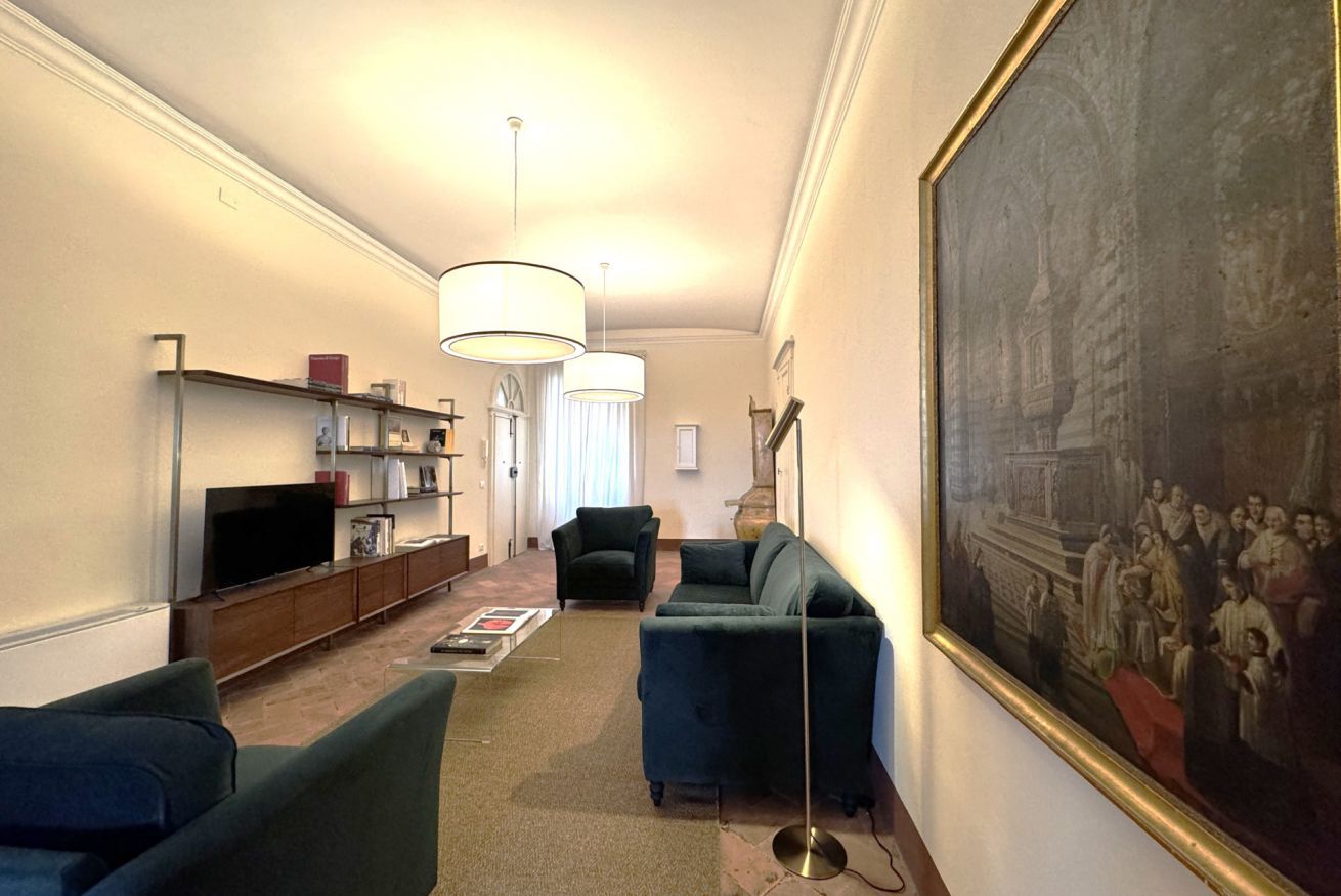 A living room with a sofa, armchair, TV, bookshelf, and a large painting on the wall.