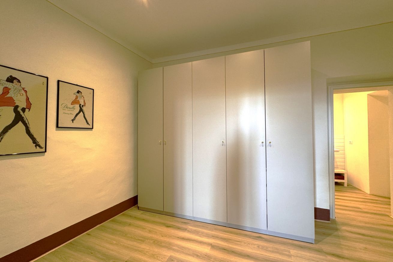Et værelse med en stor, hvid garderobe, trægulv og to billeder i rammer på væggen.
