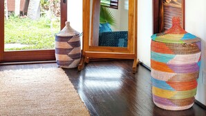 A room with a wooden floor, a large mirror, a colorful woven stool, and a woven rug. - The Palmwood  (Kilauea)