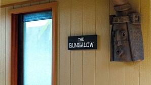 A room with a wooden door, a sign reading "The Bungalow", and a small orange bed. - The Palmwood  (Kilauea)