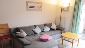 A grey sofa with pillows, a wooden chair, a small wooden table, and a framed picture on the wall. - Haus in Ostfriesland mit Garten (Dornum)