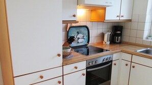A kitchen with white cabinets, a black stove, and a coffee maker. - Haus in Ostfriesland mit Garten (Dornum)