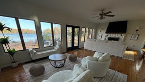 A spacious living room with large windows, a fireplace, and a ceiling fan.