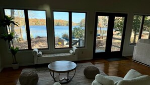 A room with large windows overlooking a lake, a round table, and white furniture.