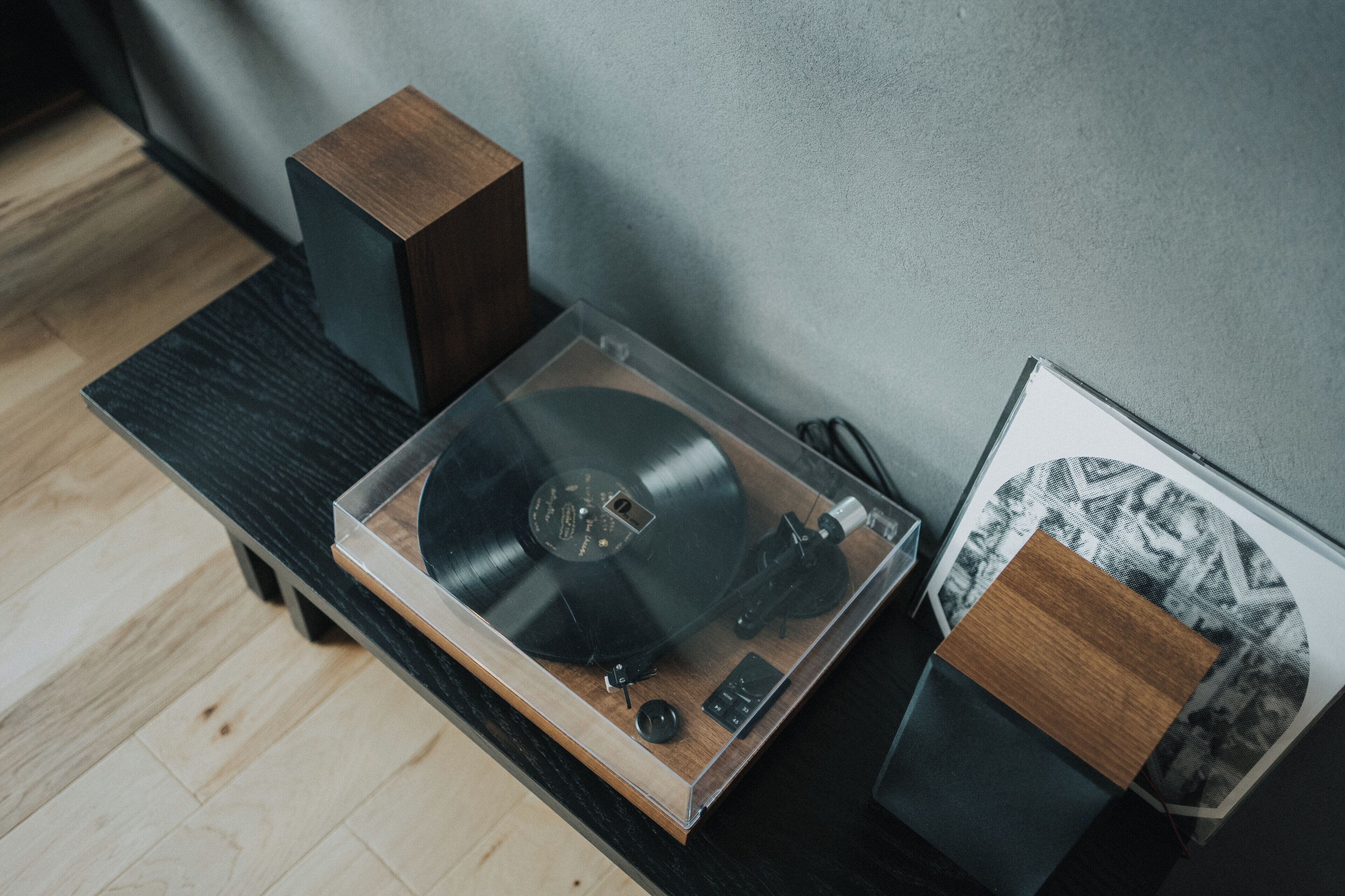 A turntable on a wooden table with speakers, a framed picture, and a patterned wall.