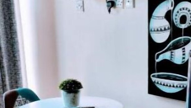 A small dining area with a round table and two chairs, a potted plant, and a flat-screen TV mounted on the wall.