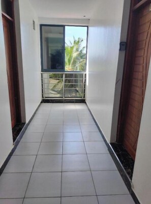 Stroll through this serene corridor to a balcony with a view of lush greenery and the sky.