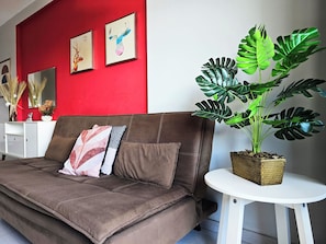 Un divano marrone con cuscini decorativi, un tavolino bianco e un'ampia pianta Monstera.