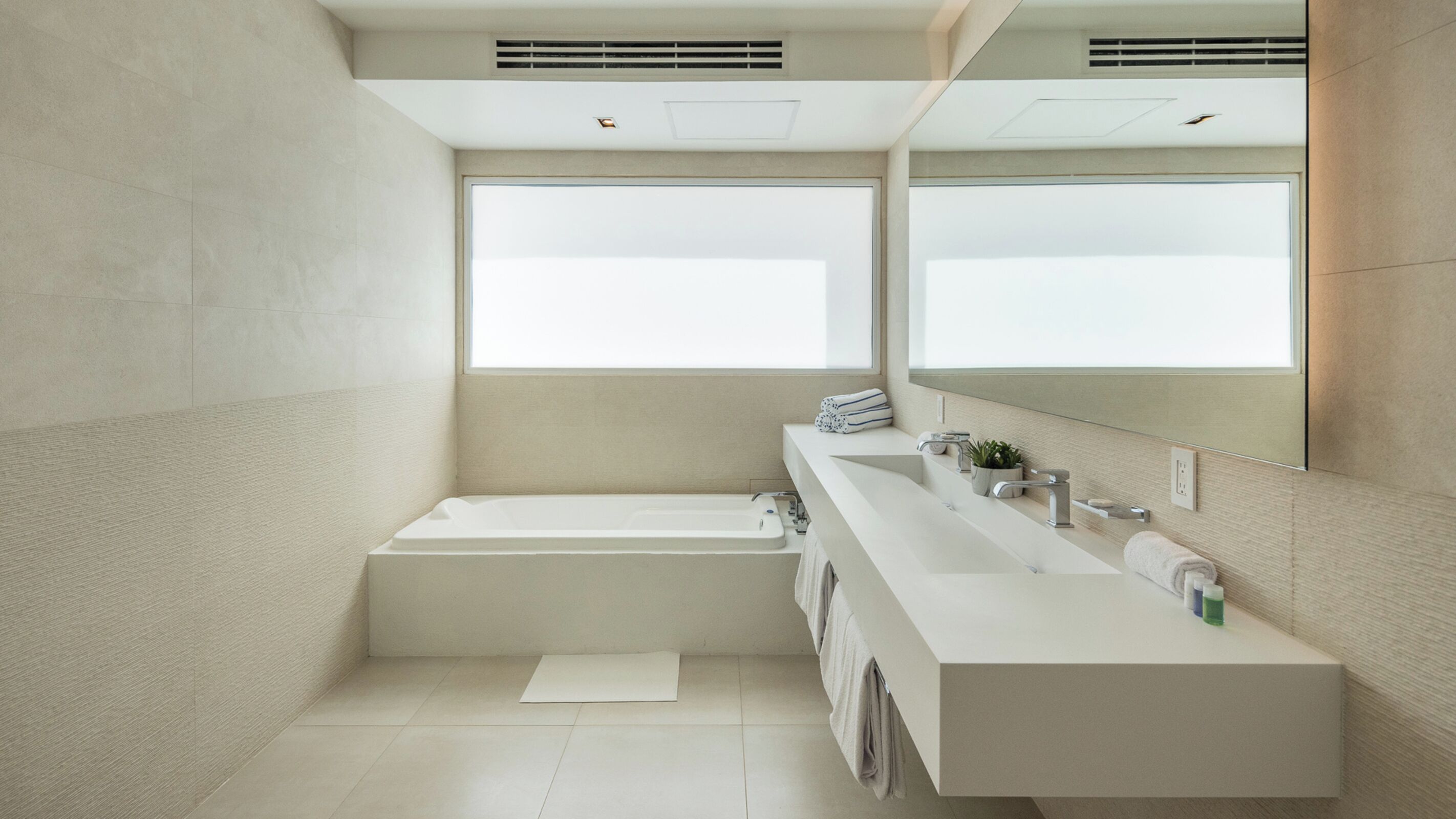 Un baño moderno con una bañera grande, un tocador espacioso con espejo y un ventanal que proporciona luz natural.