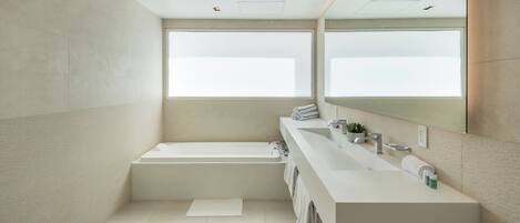 Un baño moderno con una bañera grande, un tocador espacioso con espejo y un ventanal que proporciona luz natural.