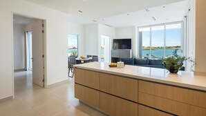 A modern kitchen with a large island, a dining area with a view of the sea, and a living area with a sofa and a TV. - Costa Divina LV 62 by Kivoya (Puerto Peñasco)
