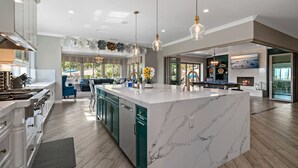 Een ruime keuken met een groot eiland, moderne apparatuur en hanglampen.