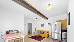 A compact living space with a dining area, a sofa, a kitchen with a refrigerator and oven, and a ceiling light fixture.