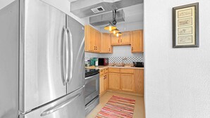 A compact kitchen with stainless steel appliances, wooden cabinets, and a colorful striped rug.