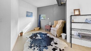 A room with a large cowhide rug, a chair, a small table, a shelf with towels, and a window with a view.