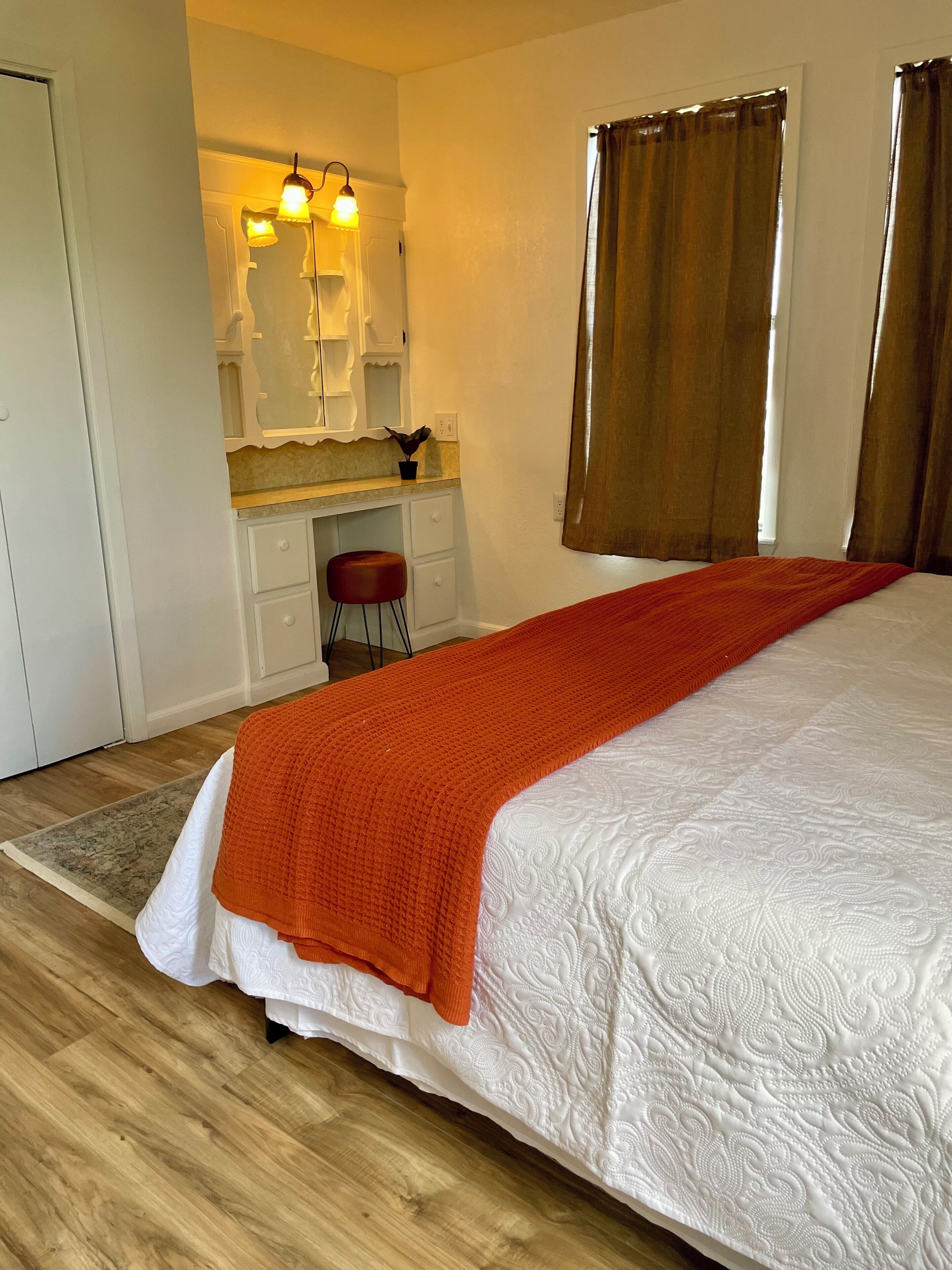 A bedroom with a bed, a desk, a chair, and a mirror.