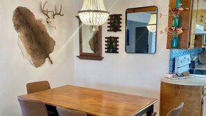 A dining area with a wooden table and four chairs, a chandelier, a mounted deer head, and a mirror on the wall.