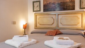 A hotel room with a large bed, two pillows, a nightstand with a lamp, and artwork on the wall. - Zero Stairs + Canal View (Venezia)