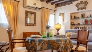 A dining area with a table set for two, surrounded by wooden chairs, a sofa, and a bookshelf. - Zero Stairs + Canal View (Venezia)