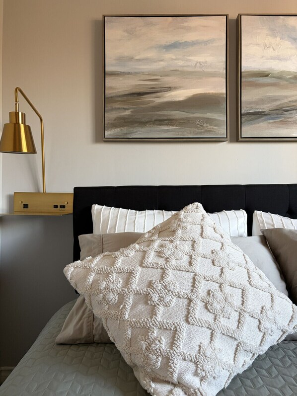 A bedroom with a bed, pillows, a bedside lamp, and two framed artworks on the wall.