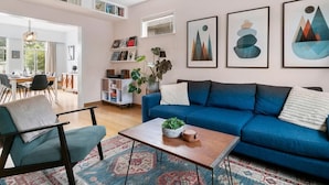 A living room with a blue sofa, a coffee table with a plant, a patterned rug, and abstract wall art. - Trout Lake Oasis - 3 bedroom (Vancouver)