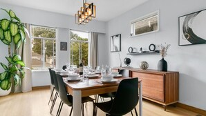 A modern dining room with a wooden table set for six, black chairs, a wooden cabinet, and a large window with curtains. - Trout Lake Oasis - 3 bedroom (Vancouver)