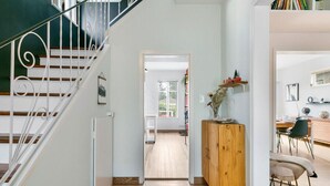 A staircase with white railings leading to a room with a wooden cabinet and a dining area with chairs and a table. - Trout Lake Oasis - 3 bedroom (Vancouver)