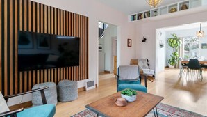 A modern living room with a flat-screen TV, a wooden accent wall, and a dining area with a table and chairs. - Trout Lake Oasis - 3 bedroom (Vancouver)