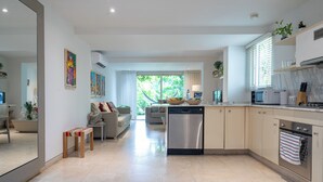 A modern kitchen with a dishwasher, microwave, and oven. There is a dining area with a table and chairs, and a sofa. The kitchen has a large window with blinds. - Best Location & Comfort in the Walled City (Cartagena de Indias)