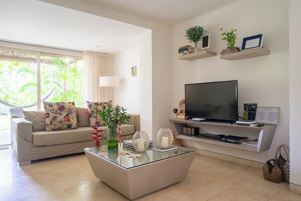 Un salon moderne avec une table basse en verre, un canapé beige et un téléviseur à écran plat.