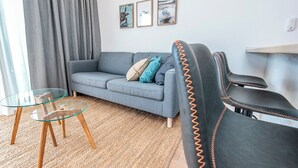 Ein Wohnzimmer mit grauem Sofa, einem Glastisch und einem Teppich. An der Wand hängen drei gerahmte Bilder.