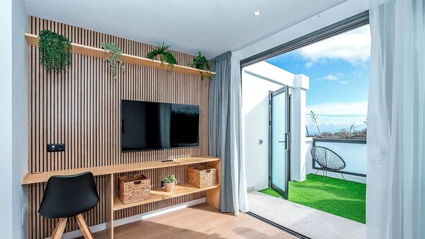 Ein modernes Wohnzimmer mit Flachbildfernseher, Holzböden und Blick auf eine grüne Rasenfläche und ein Gewässer.