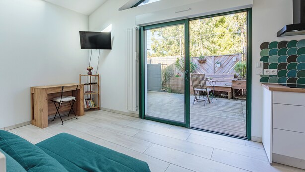 Uma sala de estar moderna com sofá, escrivaninha de madeira, TV e porta de vidro deslizante para um pátio externo.