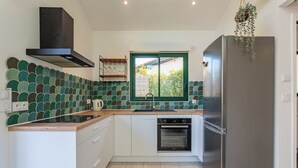 Cozinha moderna com armários brancos, geladeira de aço inoxidável, forno embutido e janela com vista para o verde.