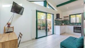 Uma cozinha moderna com televisão de tela plana na parede, uma área de refeições com mesa e cadeiras de madeira, e uma porta de vidro deslizante que dá para um pátio.