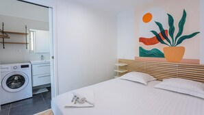 Quarto de hotel moderno com uma cama bem arrumada, máquina de lavar e uma obra de arte na parede.
