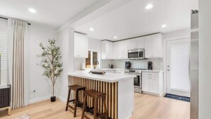 Una cocina moderna con muebles blancos, una isla central con taburetes y un horno empotrado.
