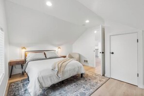 Een slaapkamer met een bed, nachtkastje, lamp en een deur.
