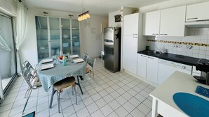 Eine kleine Küche mit weißen Schränken, einem Edelstahlkühlschrank und einem Essbereich mit Tisch für vier Personen.