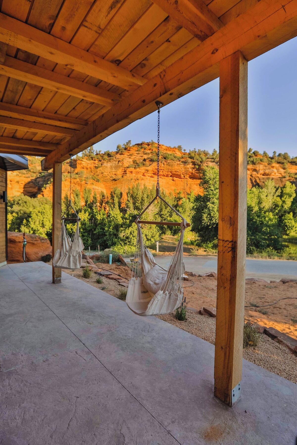A wooden pergola with two hammocks hanging from it, overlooking a scenic view of red rock formations and greenery.