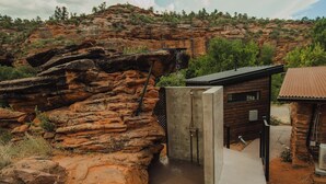 A rustic cabin with a concrete entrance, surrounded by red rock formations and sparse vegetation.